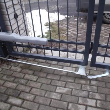 Přerušený mechanismus sekčních vrat na dlažbě s hromadou sněhu v pozadí.