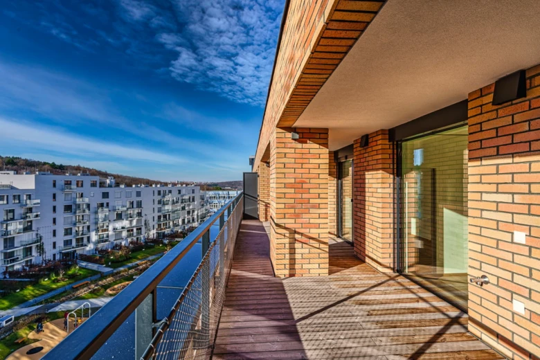 Moderní balkon s výhledem na bytový dům pod modrou oblohou.