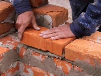 Ruční kladení cihel na maltu při stavbě zdiva.