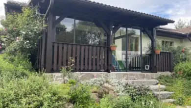 Dřevěná terasa s velkými skleněnými panely v zahradním prostředí.