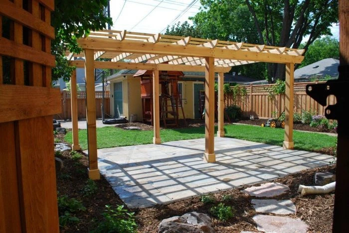 Nově postavená dřevěná pergola na kamenné terase v zahradě.