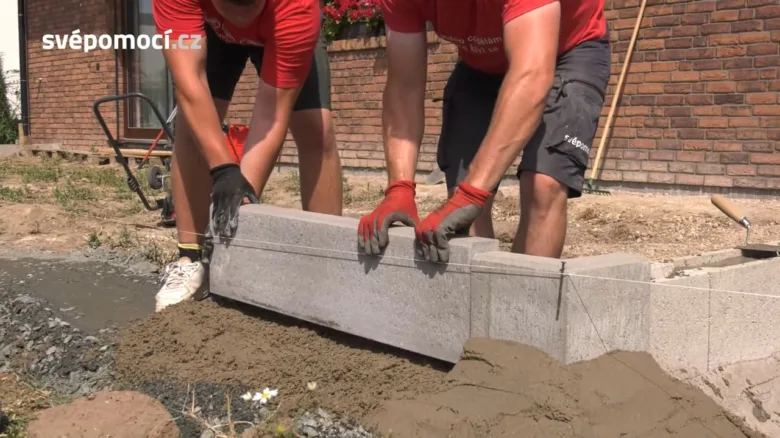 Dva muži kladou betonový obrubník na maltu.
