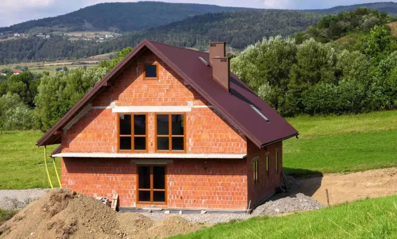 Stavba chaty z cihel na kopci s horami v pozadí.