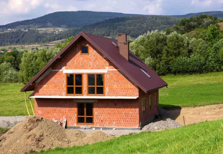 Stavba chaty z cihel na kopci s horami v pozadí.