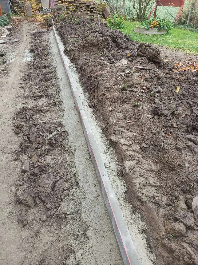 Instalace obrubníku do výkopu s viditelným betónem.