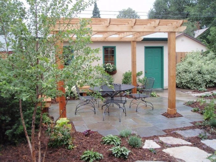 Hotová dřevěná pergola s zahradním nábytkem na kamenné terase.