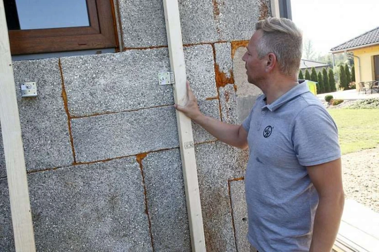 Muž montuje dřevěný rám na fasádu z kamenných bloků.