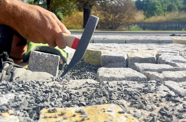 Ručník položí žulové dlažební kostky do štěrku pomocí kladiva.