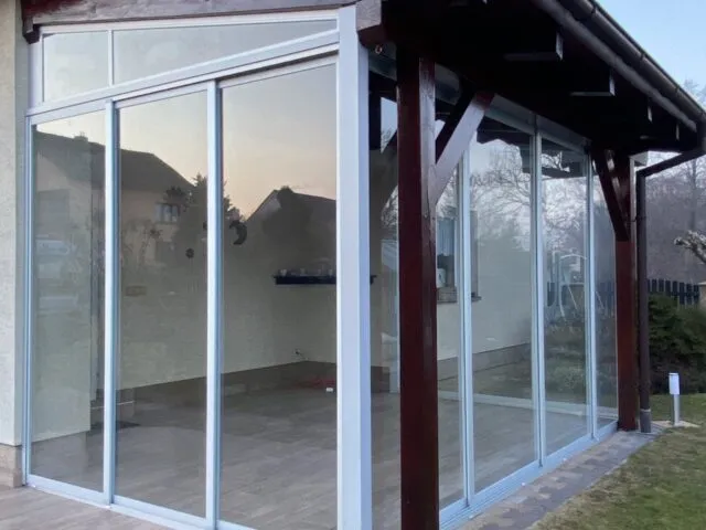 Skleněná fasáda zasklení verandy s posuvnými dveřmi a dřevěným rámem.