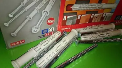Bílé hmoždinky se šrouby pro beton vedle krabice značky Klimas.