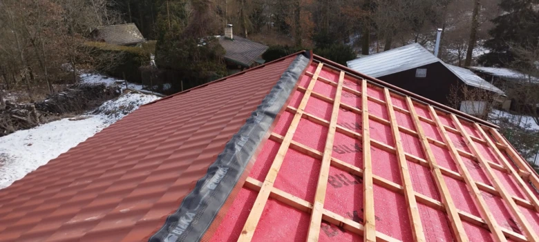Instalace střešní lepenky na dřevěné laty s červenou střechou.