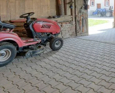 Červený traktor na dlažbě před garáží ukazuje použití dlaždíc venku.