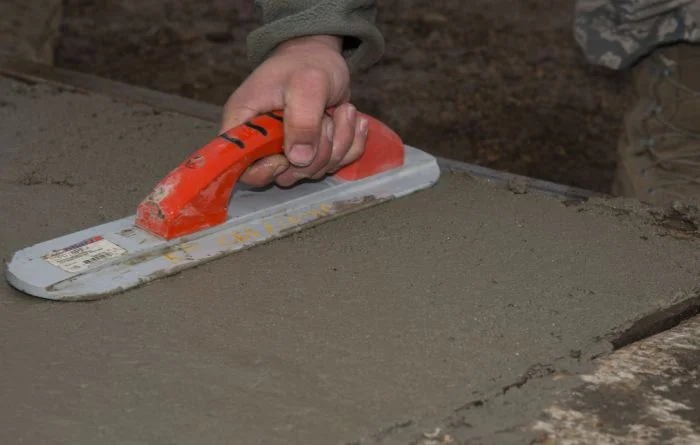 Ruka hladí čerstvý beton špachtlou při stavbě podlahy.