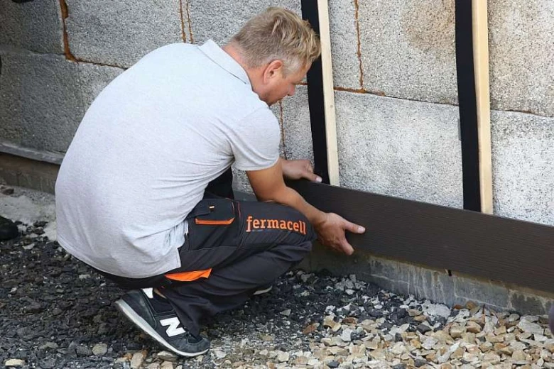 Muž montuje tmavý fasádní panel na zdivo s dřevěnými latkami.