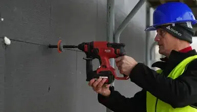 Stavebník vrtá do zdiva pomocí elektrického vrtače.
