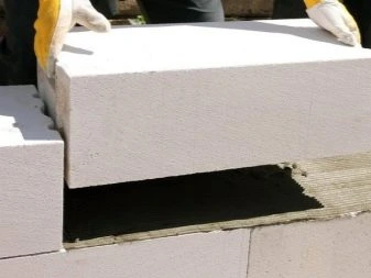 Stavebník položí blok autoklávovaného pórobetonu na maltu.