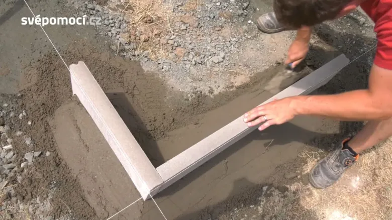 Muž pokládá obrubník do betonu pomocí pravítka.