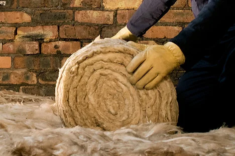 Rukou se manipuluje s válcem minerální vaty pro zateplení fasády.