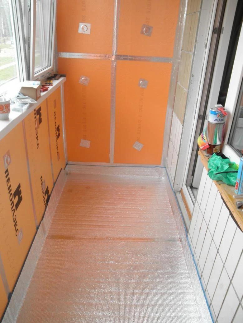 Balkon s oranžovou izolační fólií a odrazivou podlahou během stavby.