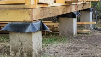 Dřevěný dům postavený na betonových pilotách s černou ochranou.