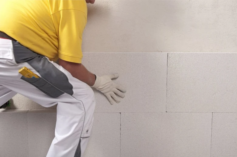 Stavebník připravuje starou omítku na zdi před renovací.
