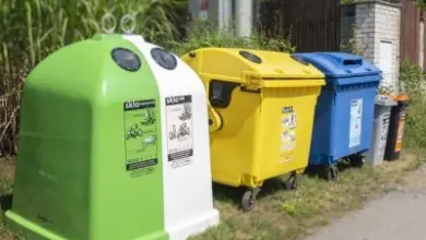 Řada barevných kontejnerů na recyklaci venku u plotu.