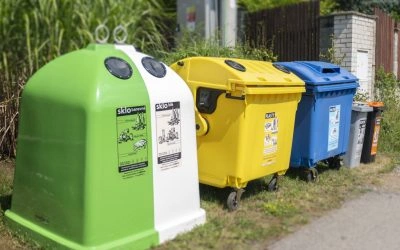Řada barevných kontejnerů na recyklaci venku u plotu.