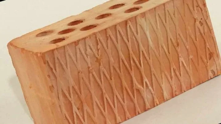 Červená cihla s otvory pro zateplování a diagonální rytím.