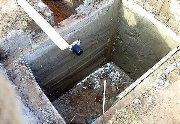 Zemní toaleta s betonovými panely a výpustním potrubím.