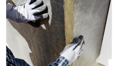 Ruce v rukavicích aplikují desku z polystyrenu na stěnu.