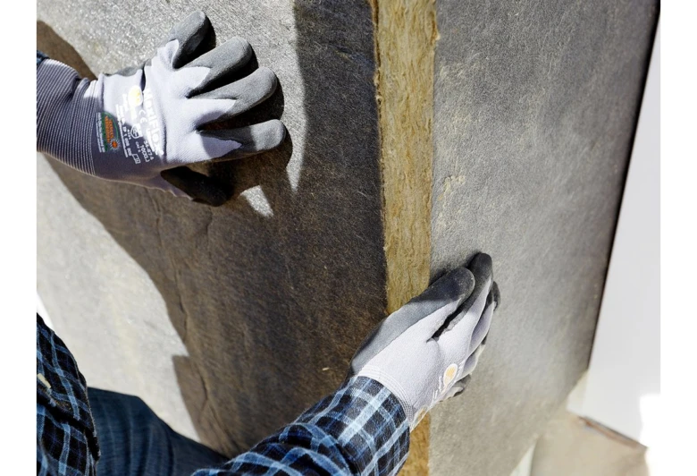 Ruční instalace izolačního materiálu mezi stěnovými trámy.