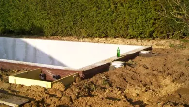 Bílá PVC fólie bazénu v jámě s okolní zemí a keři.