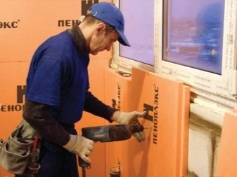 Montážní dělník připevňuje oranžové desky Penoplexu ke zdi.