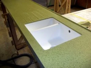 Zelená umělá kamenná pracovní deska s integrovanou bílou dřezovou vaničkou.