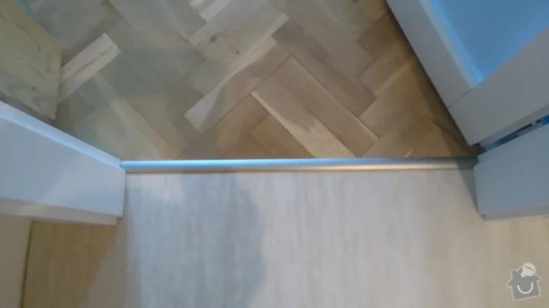 Detailní pohled na nainstalovaný kovový prah mezi dvěma typy parket.