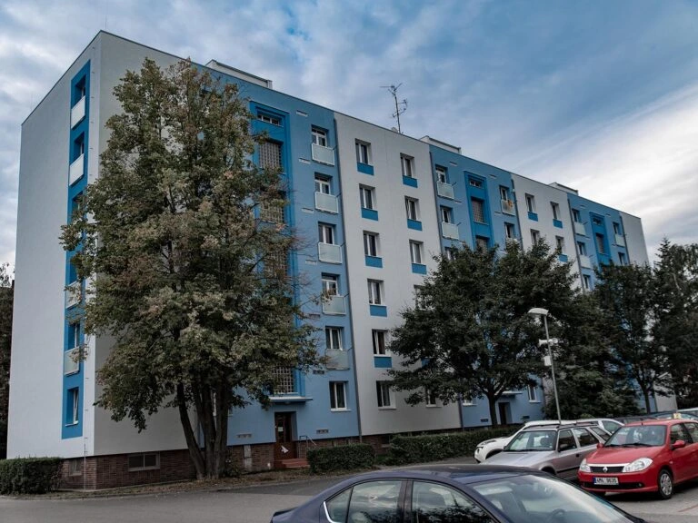Modro-bílý panelový dům s balkony v českém městě.