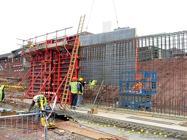 Stavebníci kontrolují betonovou stěnu s bedněním na stavbě.
