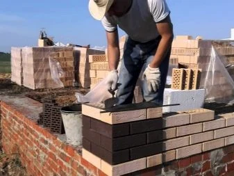 Stavebník kladne cihly na zdivo u skladu s materiálem.