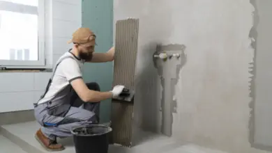 Muž nanáší lepidlo na dlaždici v koupelně.