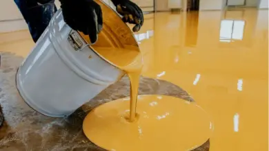 Nálev žluté podlahové barvy z kbelíku na betonovou plochu.
