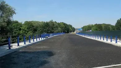 Čerstvě položený asfaltový povrch s modrými sloupky pod jasným nebem.