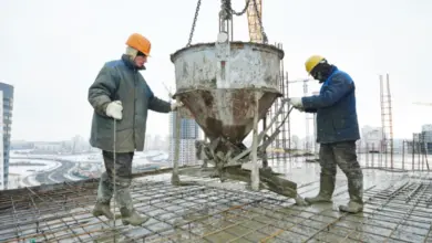 Dva dělníci nalévají čerstvý beton na ocelovou mřížku.