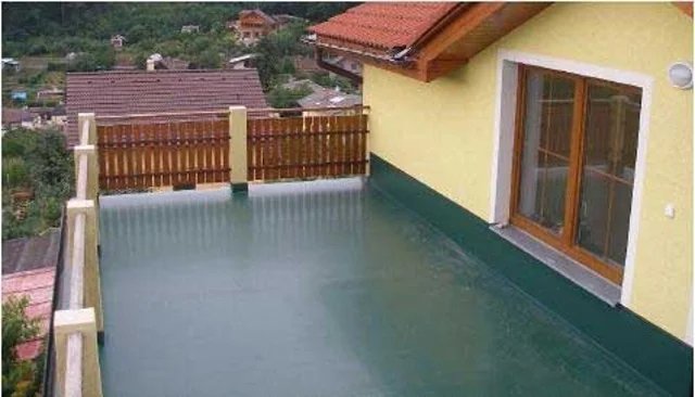 Hotový zelený povrch izolovaného balkonu u žluté fasády domu.