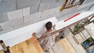 Muž připevňuje polystyrenovou desku ke zdi lepidlem na stavebním podvozku.