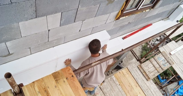 Muž připevňuje polystyrenovou desku ke zdi lepidlem na stavebním podvozku.