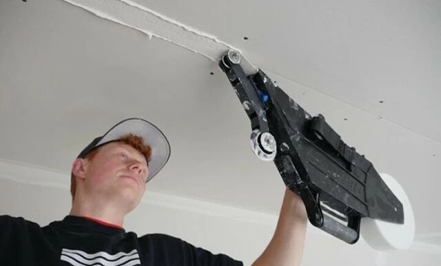 Muž nanáší lepidlo na spoji sádrokartonu stropu pomocí nástroje.