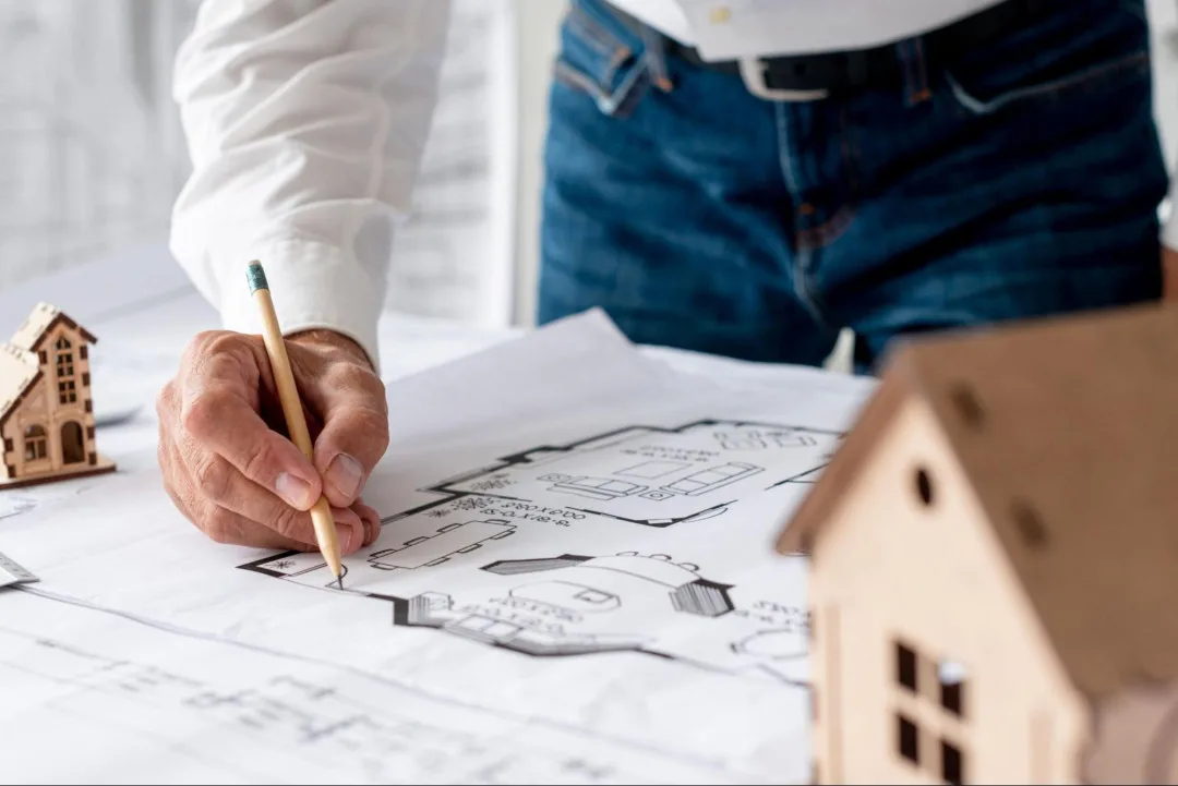 Architekt kreslí plán domu s modely pro zónování prostoru.