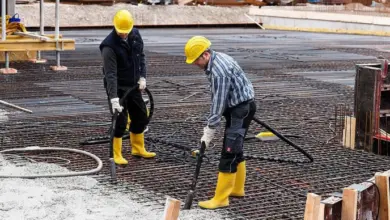 Dva dělníci vibrují beton na ocelové mřížce pro pevnost.