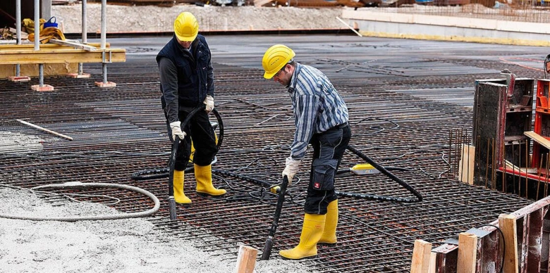 Dva dělníci vibrují beton na ocelové mřížce pro pevnost.