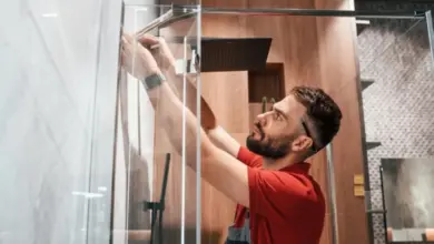 Muž instaluje skleněnou desku sprchového koutu.